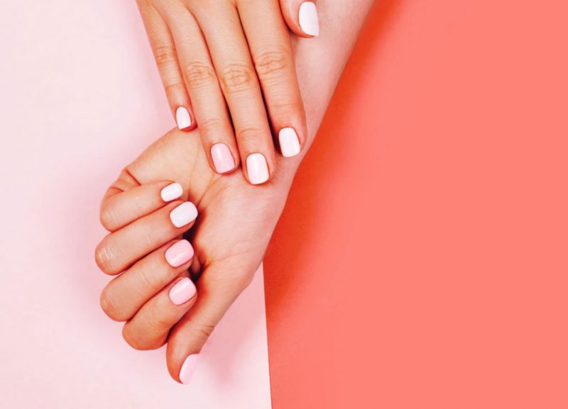 Woman's hands with pink nail polish on pink background 
