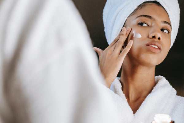 Woman in white robe and hair in white towel putting moisturiser on her face